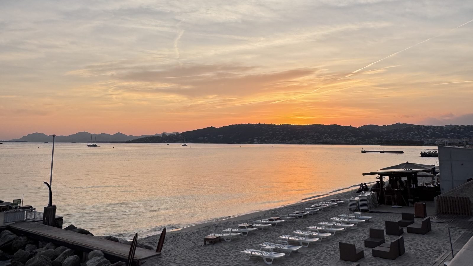 The coast in low golden October light (Baie des Anges or Cap d'Antibes), a few people, calm sea.